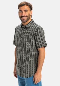 Camisa negra de manga corta con rayas verticales blancas y patrones florales, con cuello y un bolsillo en el lado izquierdo del pecho.