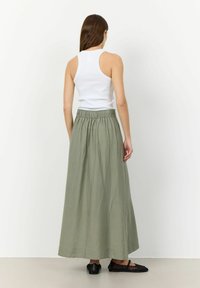 Top blanco sin mangas y falda maxi verde oliva con cintura elástica, que presenta una tela ligera y una textura suave. Sandalias planas negras.