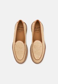 Beige flettede slip-on sko i loafermodell med brun trim og lærsåler, vist ovenfra på en hvit bakgrunn.
