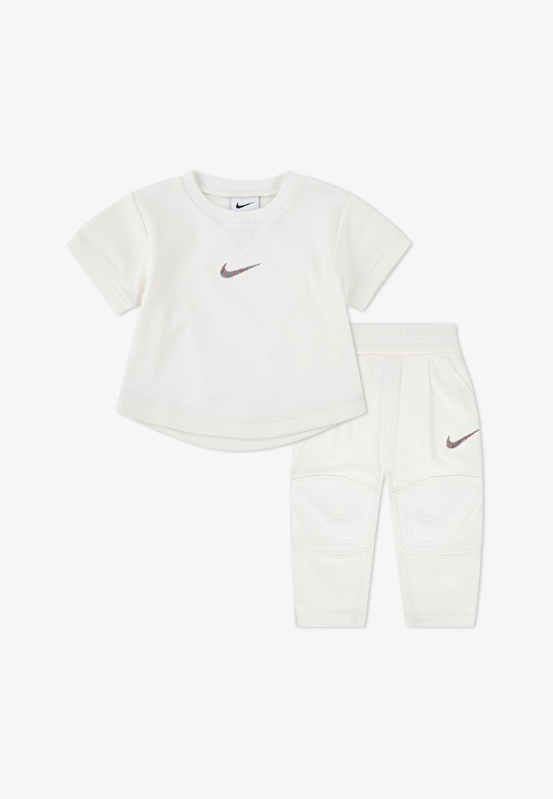 White Nike two-piece set featuring a short-sleeve top with a small logo and pants with textured accents and side pockets.