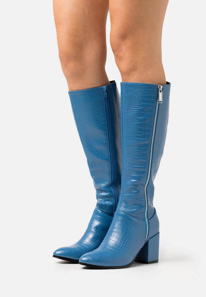 Bottes montantes en cuir synthétique bleu effet crocodile, avec un bout pointu, un talon bloc et une fermeture éclair latérale. Texture lisse avec une finition brillante.