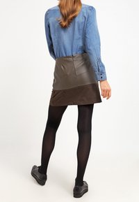 Schicker zweifarbiger Rock mit einem braunen strukturierten Stoff und einem glatten, dunkeloliven Kunstlederpanel. Kombiniert mit schwarzen blickdichten Strumpfhosen und Schuhen.