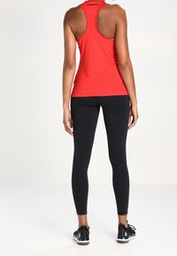 Rode atletische tanktop met racerback-ontwerp, gecombineerd met zwarte leggings en zwarte sportschoenen, met een nauwsluitend silhouet.