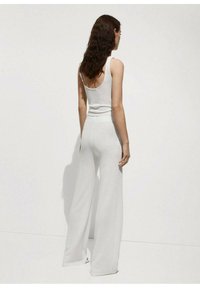 Top in cotone bianco a coste abbinato a pantaloni larghi e fluenti. L'outfit presenta un tessuto strutturato e una vita aderente.