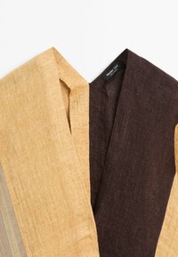 Close-up of a two-tone beige and dark brown textured fabric garment with a V-neck and Massimo Dutti label.