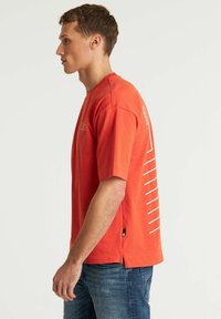 T-shirt di cotone rosso con maniche corte, colletto a girocollo e motivo a linee bianche sul lato sinistro, con spacchi laterali all'orlo.