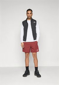 Miesten asu koostuu mustasta hihattomasta liivistä, valkoisesta pitkähihaisesta paidasta, viininpunaisista shortseista ja mustista urheilukengist�ä. Liivissä ja shortseissa näkyy huomattava merkin logo.