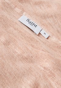 Jasnoróżowy sweter dzianinowy z luźnym splotem, z białą metką z napisem "Saint Tropez" oraz rozmiarem "M" w czarnym tekście.