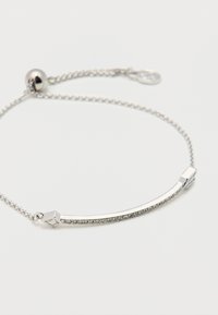 Ασημένιο βραχιόλι με καμπύλη μπάρα που διαθέτει μικρά διάφανα κρυστάλλινα στοιχεία και λεπτή αλυσίδα με ρυθμιζόμενο κούμπωμα ολισθητήρα σε λευκό φόντο.