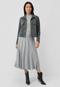 Szara kurtka w jodełkę o skróconym kroju z dwoma przednimi kieszeniami, zestawiona z jasnoszarą plisowaną spódnicą midi i czarnymi skórzanymi botkami na wysokim obcasie.