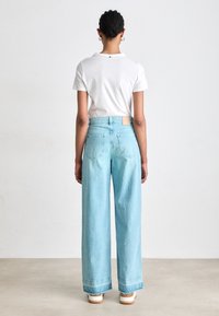 Lyse blå vide jeans med en frynset kant og to baklommer, sammen med en enkel hvit T-skjorte. Minimalistisk design, uten bemerkelsesverdige mønstre.