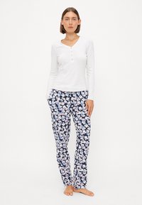 Haut à manches longues blanc avec patte de boutonnage, associé à un pantalon floral bleu marine orné de fleurs rose clair et blanches, fabriqué en tissu léger.
