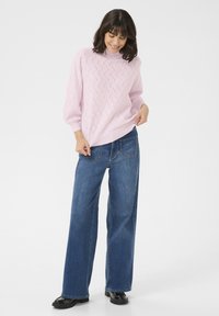 Maglione rosa chiaro lavorato a maglia con un motivo testurizzato, abbinato a jeans in denim blu a gamba larga e mocassini neri lucidi.