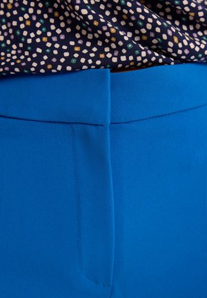 Niebieskie spodnie o gładkiej teksturze i prostym kroju. Pas znajduje się na górze, z subtelnymi akcentami w postaci przeszyć. Powyżej widoczny jest wzorzysty materiał.