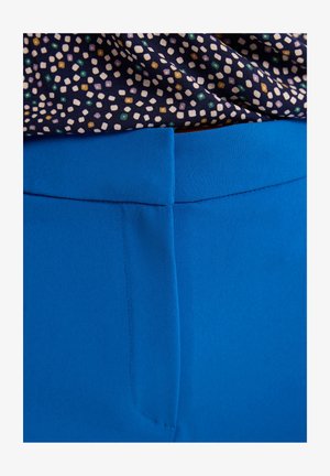 Niebieskie spodnie o gładkiej teksturze i prostym kroju. Pas znajduje się na górze, z subtelnymi akcentami w postaci przeszyć. Powyżej widoczny jest wzorzysty materiał.