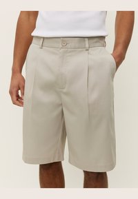 Beige plisserte shorts laget av glatt stoff, med sidelommer og knappelukking, tilpasset for en avslappet passform.