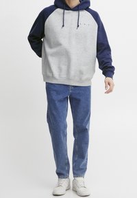 Grå og marineblå color-blocked hættetrøje med snoretræk i hætten, med frontlomme, kombineret med lyseblå jeans og hvide sneakers.