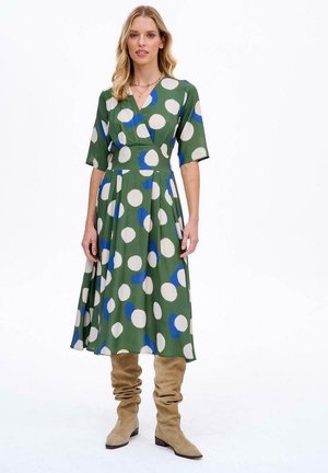 Zielona sukienka z krótkimi rękawami, z dużymi białymi i niebieskimi kropkami. Tkanina ma gładką fakturę, w zwiewnym kształcie w literę A.