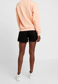 Outfit bestaande uit een perzikkleurige trui en zwarte korte broek. De trui heeft een losse pasvorm en geribbelde manchetten, terwijl de korte broek zacht en los zit. Witte sneakers maken de look compleet.