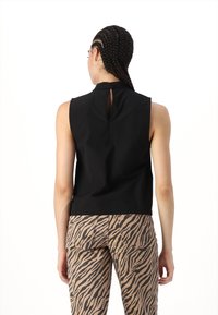 Top sans manches noir avec un col haut et un dos en clé, associé à un pantalon beige avec un motif rayé tigre noir.