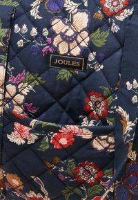 Torba z pikowanego materiału w ciemnoniebieskim kolorze, z kwiatowymi wzorami w odcieniach czerwieni, różu i fioletu. Posiada kieszeń i złotą metkę z napisem "JOULES".