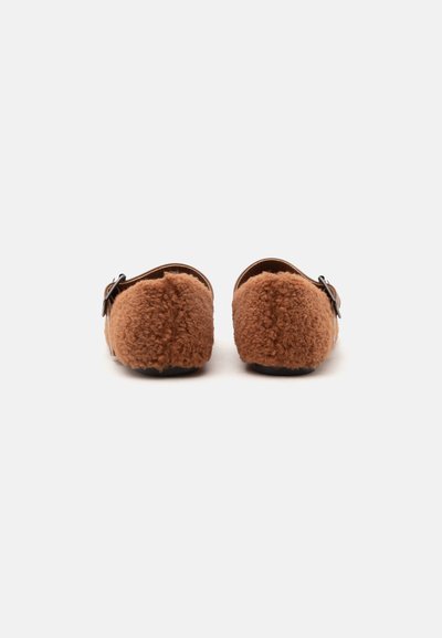 Sabots marron doux et duveteux à enfiler avec boucles réglables, vus de dos sur fond blanc.