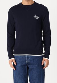 Sweat-shirt bleu marine à col rond, poignets et ourlet côtelés. Présente un logo blanc imprimé sur la poitrine et un matériau en maille texturée.
