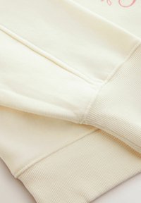 Cremfarbener Sweatshirt mit gerippten Bündchen, weicher Textur und glattem Körper. Verfügt über ein dezentes Druckdesign auf der Vorderseite.