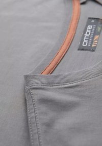 Camiseta de algodón gris con un cuello redondo y un ribete marrón en contraste, que presenta una textura acanalada y detalles de costura cuidados.