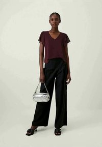 Top corto rossa, pantaloni neri a gamba larga, sandali neri, in mano una borsa silver con catena. Tessuto liscio, vestibilità comoda.