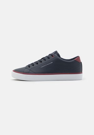 Baskets basses bleu marine avec semelle blanche, bord rouge, lacets noirs et logo "Tommy Hilfiger" sur le côté et la languette du talon.
