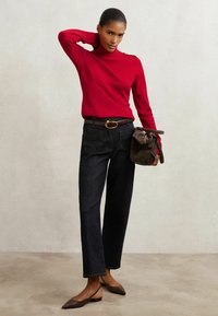 Maglione a collo alto rosso con dettagli sulle spalle, jeans in denim scuro a gamba dritta, cintura marrone e borsa in pelle marrone. Mocassini con punta.