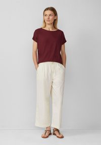 Haut bordeaux à manches courtes associé à un pantalon crème ample et des sandales marron avec une sangle à motif léopard.