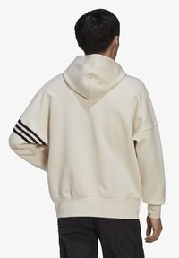 Felpa color crema con un ampio cappuccio, vestibilità ampia e tre strisce nere sulla manica sinistra. Tessuto morbido e polsini a coste.