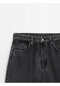 Jean en denim noir taille haute avec fermeture bouton en métal, poches avant et passants de ceinture sur fond blanc.