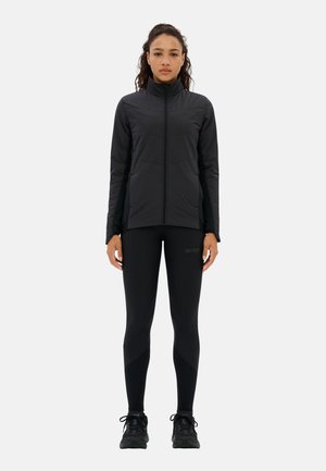 Schwarze Sportjacke mit hohem Kragen und Reißverschluss, kombiniert mit schwarzen Leggings mit strukturierten Akzenten. Die Schuhe sind schwarze Sportschuhe.