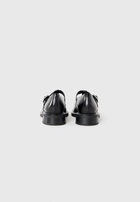 Black leather shoes with a smooth finish, round toe, and low, textured heel. Features a strap and buckle detail at the ankle.