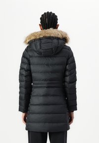 Crna puffer jakna s umjetnim krznom na ovratniku, s kvadratnim šavovima, dužine do sredine bedara i dugim rukavima. Glatka tekstura s prilagođenim siluetom.