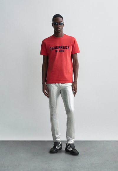 Punane puuvillane T-särk musta "DSQUARED2 MILANO" trükiga, koos läikivate hõbedaste kitsaste teksade ja mustade kingadega, millel valged triibud.