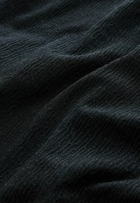 Zbliżenie ciemnej tkaniny o subtelnym prążkowanym wzorze i delikatnych fałdach tworzących miękkie cienie.