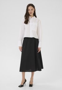 Bela srajca s kratkimi rokavi in žepom na prsih, skrajšana zasnova, v kombinaciji s črno dolgo in ohlapno krilo ter črnimi visokimi petami.