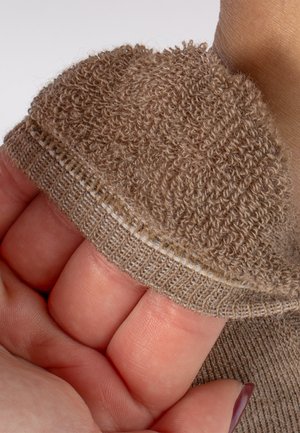 Ręka trzymająca brzeg beżowej mikrofibrowej lub frotowej rękawicy z teksturowaną, pętlową tkaniną i żebrowanym przeszyciem na szwie.