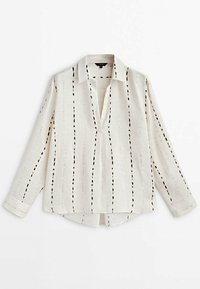 Camicia bianca in lino con una vestibilità comoda, caratterizzata da punti neri allungati disposti in linee verticali, un colletto e maniche lunghe con polsini a bottone.