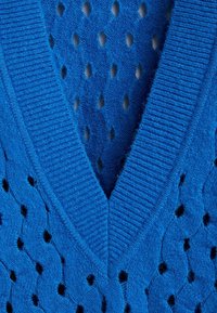 Niebieski sweter dzianinowy z dekoltem w serek, ozdobiony ażurowymi wzorami w kształcie diamentów i prążkowanymi brzegami. Miękka faktura o lekkim wyglądzie.