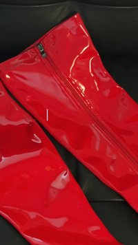 Botas altas de muslo brillantes y rojas con una textura suave, que cuentan con una cremallera central y un diseño elegante y ajustado sobre un fondo oscuro.