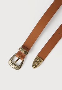 Καφέ δερμάτινη ζώνη με περίτεχνη παλιά αγκράφα από ορείχαλκο, θηλιά και άκρο που παρουσιάζουν λουλουδάτα και φυλλώδη σχέδια σε λευκό φόντο.