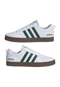 Baskets blanches en matériau synthétique, avec trois bandes vertes, un bout arrondi et une semelle extérieure en caoutchouc marron. Logo de la marque sur le côté.