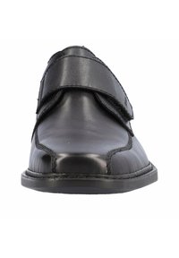 Chaussure en cuir noire avec un bout rond, dotée d'une sangle Velcro et de coutures contrastantes le long de la couture et de la semelle. Texture lisse sur toute la surface.