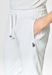 Pantaloni jogger bianchi in morbido tessuto, dotati di vita elasticizzata, cordoncini e un piccolo dettaglio logo scuro sulla coscia.