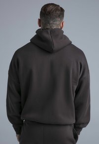 Mörkgrå huvtröja med rymlig huva, lös passform och långa ärmar. Mjuk textur utan synliga mönster eller metalldetaljer.